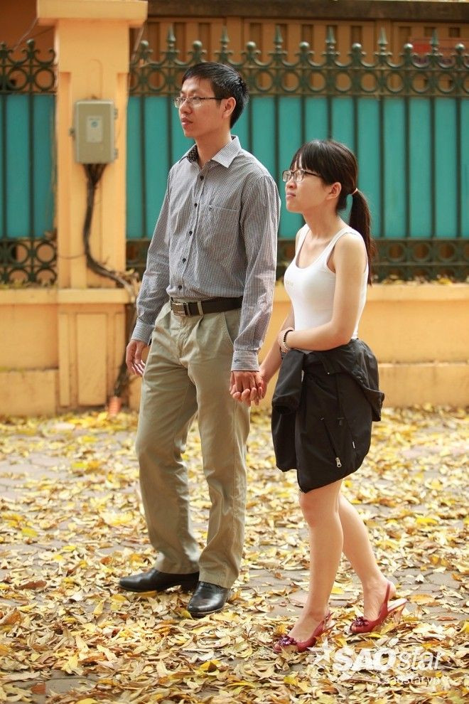 Cặp tình nhân nắm chặt tay nhau đi trên con đường đầy lá.