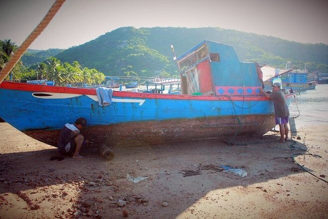 Sáu Thanh và Hai Mạnh tranh thủ cạo xác hà bên mạn thuyền râm mát khi mặt trời dần lên cao.