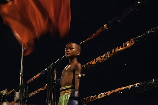 Đấm bốc Kun Khmer là một trong những cách thoát nghèo ở vùng nông thôn Campuchia. Quá trình tuyển chọn sẽ lựa ra những đứa trẻ từ 6-12 tuổi có ngoại hình ổn và tư cách đạo đức tốt. Chúng được trả từ 7 đến 10 USD cho mỗi trận thắng. Trong ảnh là Vuth Seyha, em đang đứng chờ giữa 2 hiệp đấu.