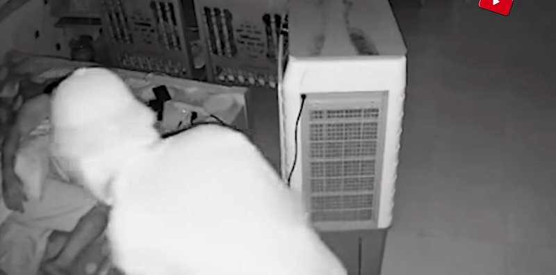 Nghe điện thoại của chủ nhà báo chuông, người đàn ông lạ mặt vội lùi về sau để ẩn nấp sau cây quạt điều hoà. Ảnh cắt từ clip