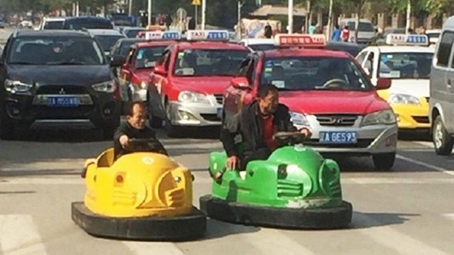 Hai người đàn ông Trung Quốc hồn nhiên lái xe điện tí hon trên phố