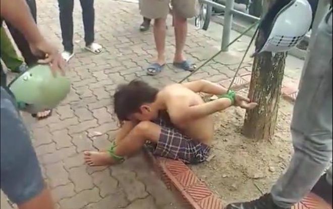 Cậu bé đánh giày cởi trần bị trói hai chân hai tay vào gốc cây gây xôn xao