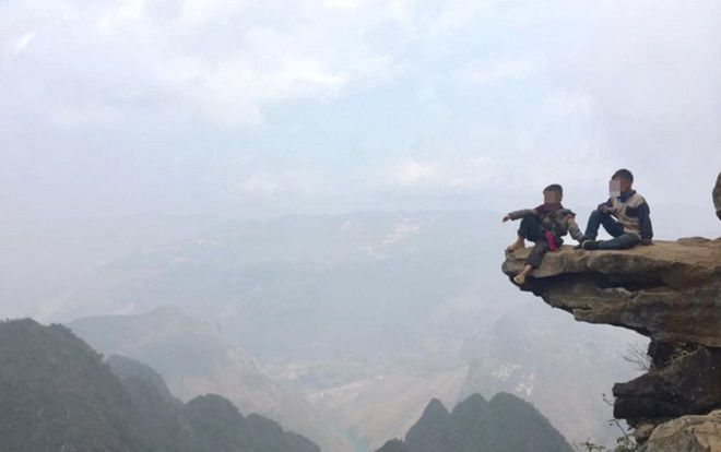 Hai đứa bé ngồi vắt vẻo trên mỏm đá cao treo leo ở Hà Giang để ‘thu tiền’ check-in khách du lịch