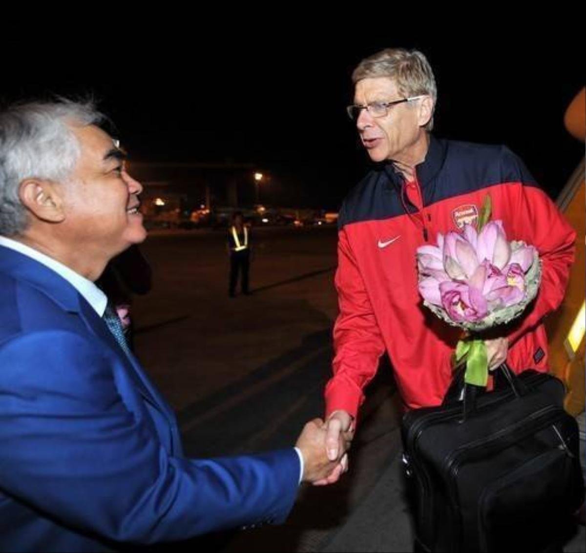 HLV Arsene Wenger được đón tiếp ngay tại chân máy bay với nón lá và hoa sen mang đặc trưng của Việt Nam.