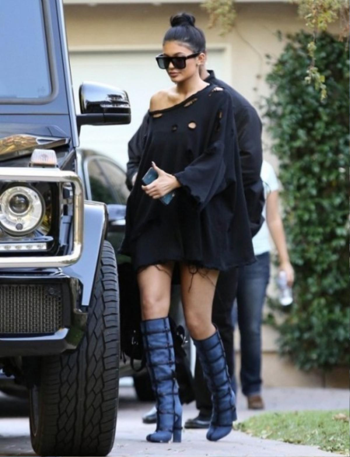 Cô em Kylie Jenner lại bụi bặm với áo oversized rách sờn chỉ nhưng không kém phần nữ tính với vai chéo. Nữ người mẫu này diện một đôi boots màu xanh dương cuốn hút.