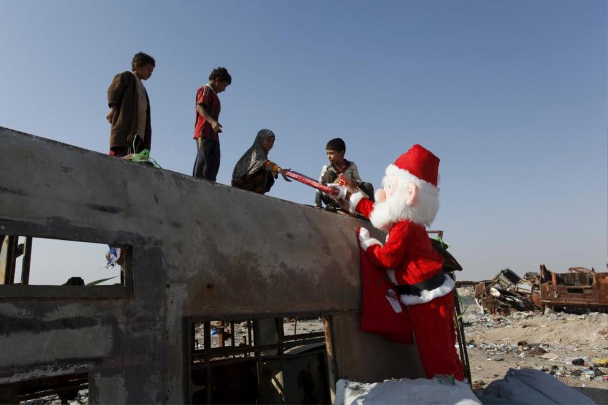 A volunteer wearing Santa Claus costume distributes presents to children at a poor community in Najaf, south of Baghdad, December 19, 2015. REUTERS/Alaa Al-Marjani