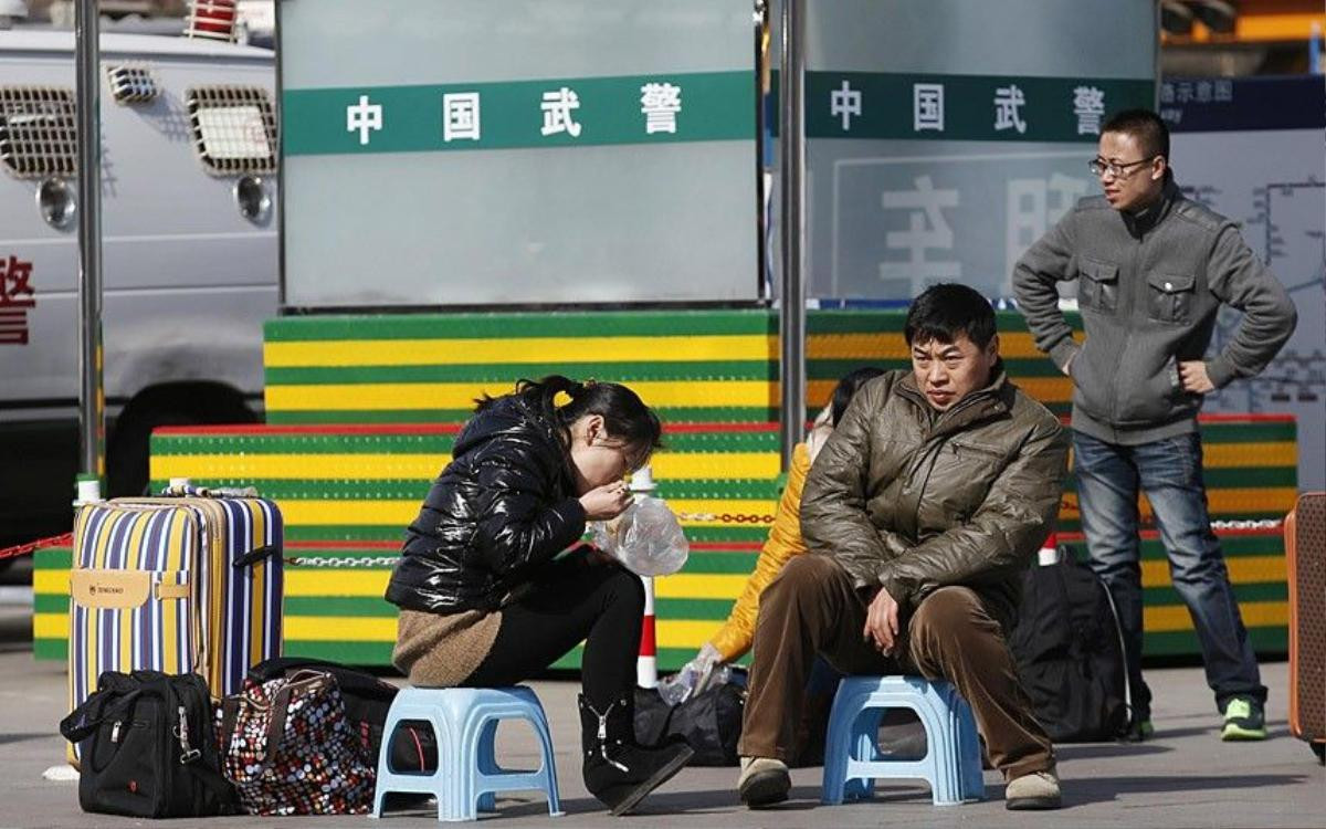 People sit on stools as they wait for their trains in front of paramilitary policemen at a railway station in Beijing February 16, 2015. Chinese Ministry of Transport said a total of 2.807 billion trips are expected to be made during the 40-day Spring Festival travel rush, which started on February 4 and will last until March 16, Xinhua News Agency reported. REUTERS/Kim Kyung-Hoon (CHINA - Tags: TRANSPORT SOCIETY)