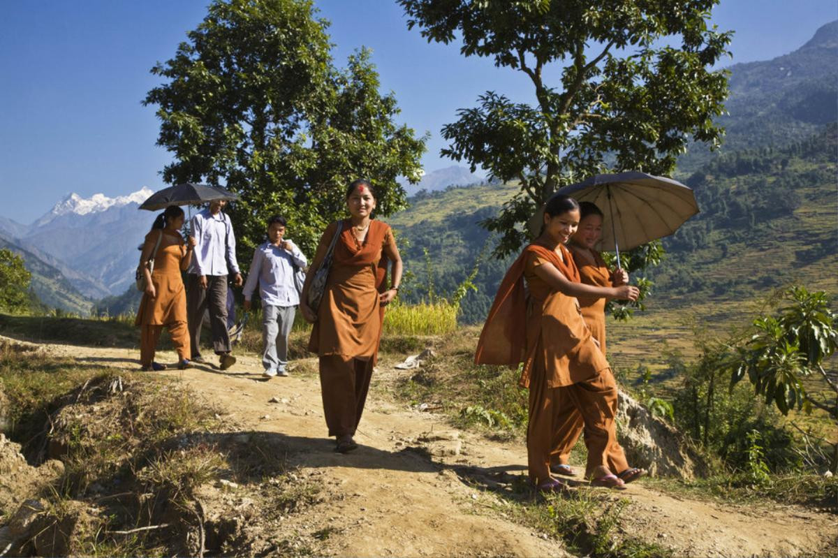 Các nữ sinh trong đống phục màu cam đang đi qua những ngọn đồi cao để tới trường ở Manaslu, Nepal.