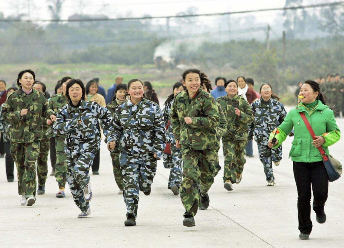 CHENGDU, CHINA: A class of girl students runs during a physical training exercise at the temporary campus of the "Walking School" of Xu Xiangyang Education and Training Group, 22 December 2005, on the outskirts of China's southwestern city of Chengdu. Some 215 boys and girls from eight to eighteen who are considered "uneducateable" students dress in camouflage jackets, sleep in trucks, study in tents, eat in the open and receive quasi-military management and physical training, culture and technology education at the boarding school. The school and families attempt to foster the children's good behaviour, independence, and the capability of studying through an "ascetic" way. AFP PHOTO/ LIU Jin (Photo credit should read LIU JIN/AFP/Getty Images)