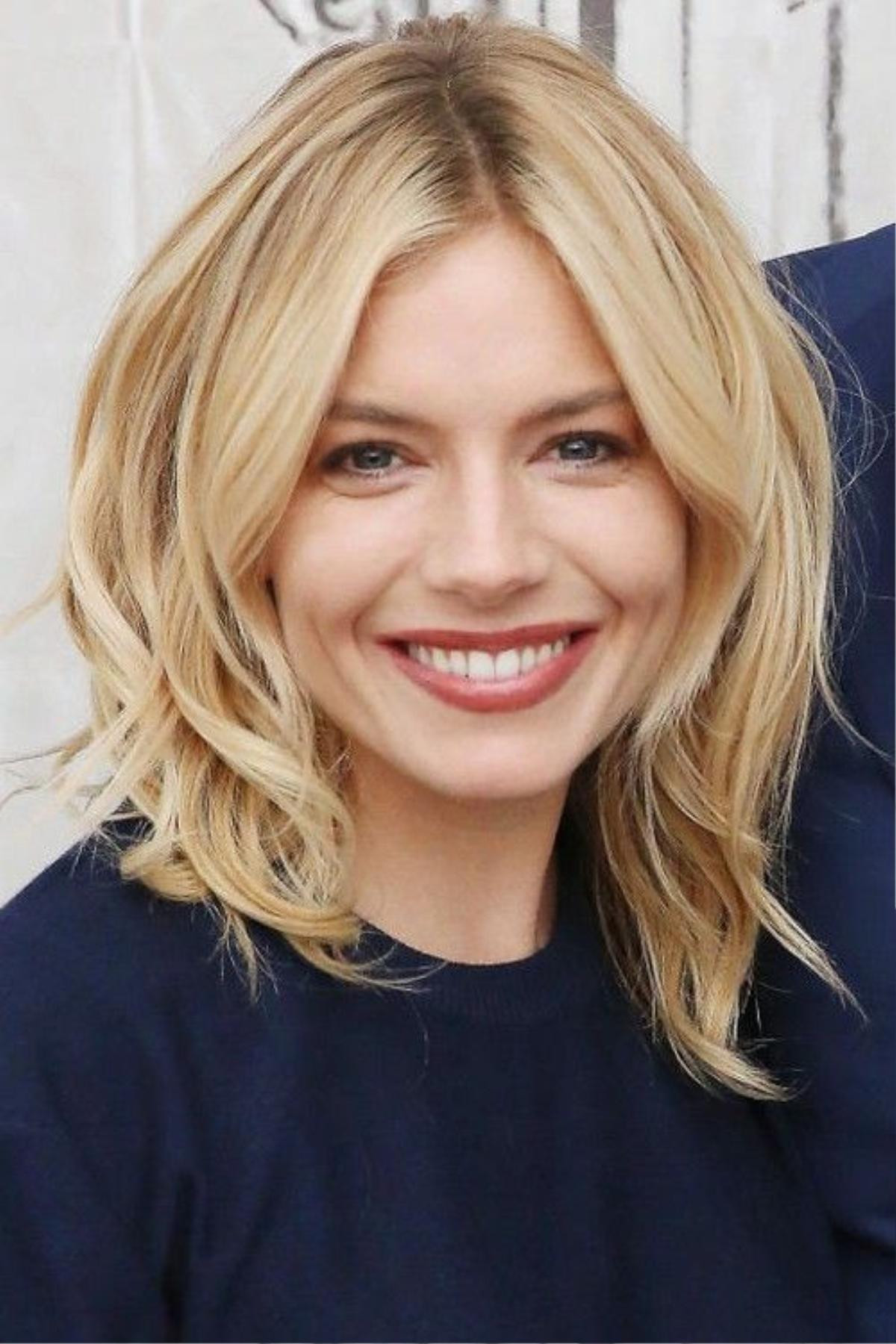 Sienna Miller chọn tóc xoăn dài chạm vai với tạo kiểu xoăn tròn, ngôi giữa.