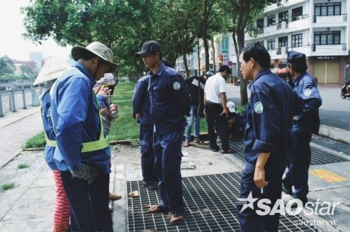 Những nhân viên môi trường đang đứng quanh khu vực cống của kênh Nhiêu Lộc, bên dưới là rất nhiều xác cá đã chết và đang có hiện tượng trương phình lên.