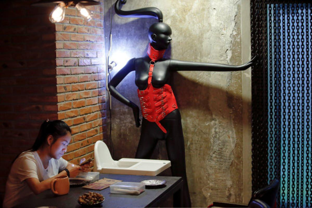 A woman uses a phone at Ke'er restaurant (Shell in English) in Beijing, China, May 26, 2016. With drinks served in breast-shaped cups and beers opened with bottle openers shaped like a wooden penis, the father and daughter team behind a Beijing S&M restaurant are encouraging customers to mix food with sex. Owner Lu Lu said business has been good since opening just under a year ago, with young Chinese streaming in to feast on seafood, such as lobster, under the gaze of mannequins wearing bondage gear. REUTERS/Kim Kyung-Hoon SEARCH "BEIJING SHELL" FOR THIS STORY. SEARCH "THE WIDER IMAGE" FOR ALL STORIES.