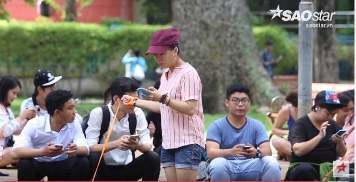 Một bạn nữ vừa dắt chó đi dạo vừa chơi Pokemon Go