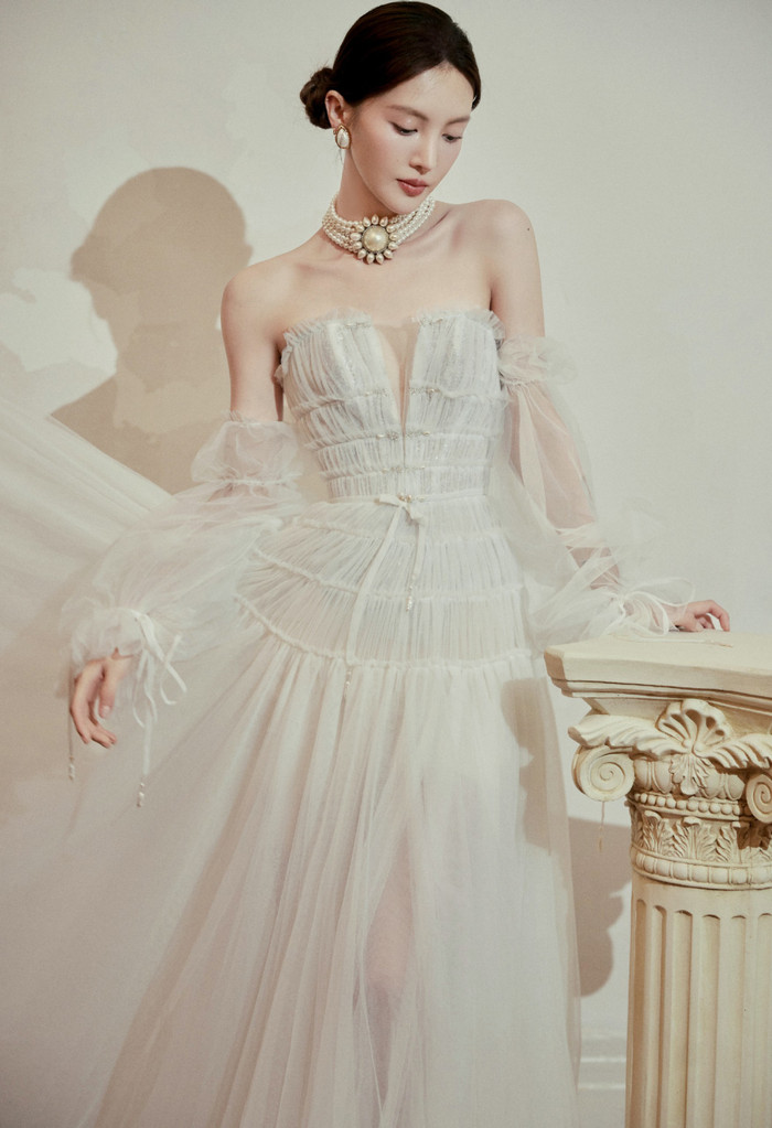 Mẫu váy khiến người xem không thể “rời mắt” khi kết đôi giữa ngực áo xẻ sâu chữ V cùng loạt chi tiết xếp ly phân tầng trên nền vải tuyn bồng bềnh. Không những vậy, outfits đặc biệt thu hút với điểm nhấn ấn tượng ở phần tay áo bo chun “đính kèm” cùng chất liệu.