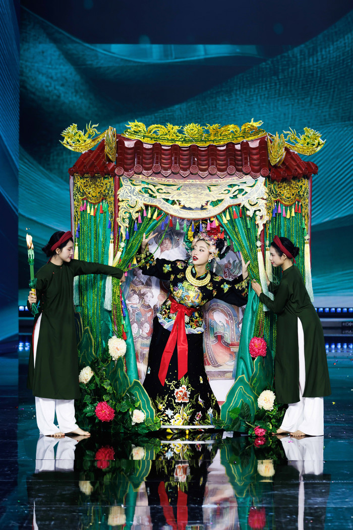 Hoa hậu Lương Thùy Linh tô son đỏ diện trang phục 'Ánh Đuốc Trên Ngàn'. Bộ cánh được khơi nguồn sáng tạo từ tín ngưỡng thờ mẫu Việt Nam, được lấy ý tưởng từ Cô Bé Đông Cuông - vị thánh cô linh thiêng chốn thượng ngàn. Tác giả muốn gửi gắm thông điệp gìn giữ, phát huy nét đẹp của tín ngưỡng thờ Mẫu và góp phần khẳng định giá trị độc đáo, đặc sắc và sức sống của di sản văn hóa đại diện cho nhân loại.