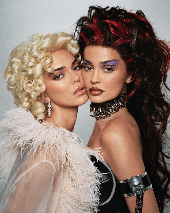 Kendall Jenner (trái) mặc một bộ đồ lót ren trắng hở sâu với tất và dây đeo quần cùng màu kèm một chiếc váy dài bán trong suốt viền lông vũ ở trên. Cô đội lại bộ tóc giả màu vàng xoăn khi hóa trang thành Marilyn Monroe. 