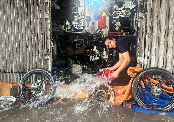 Một tiệm sửa xe máy trong tình trạng ngập nước. Thợ phải dùng bạt, dụng cụ xe máy để ngăn nước tràn vào, đồng thời cố gắng tát nước ra khỏi cửa tiệm - Ảnh: Thanh niên