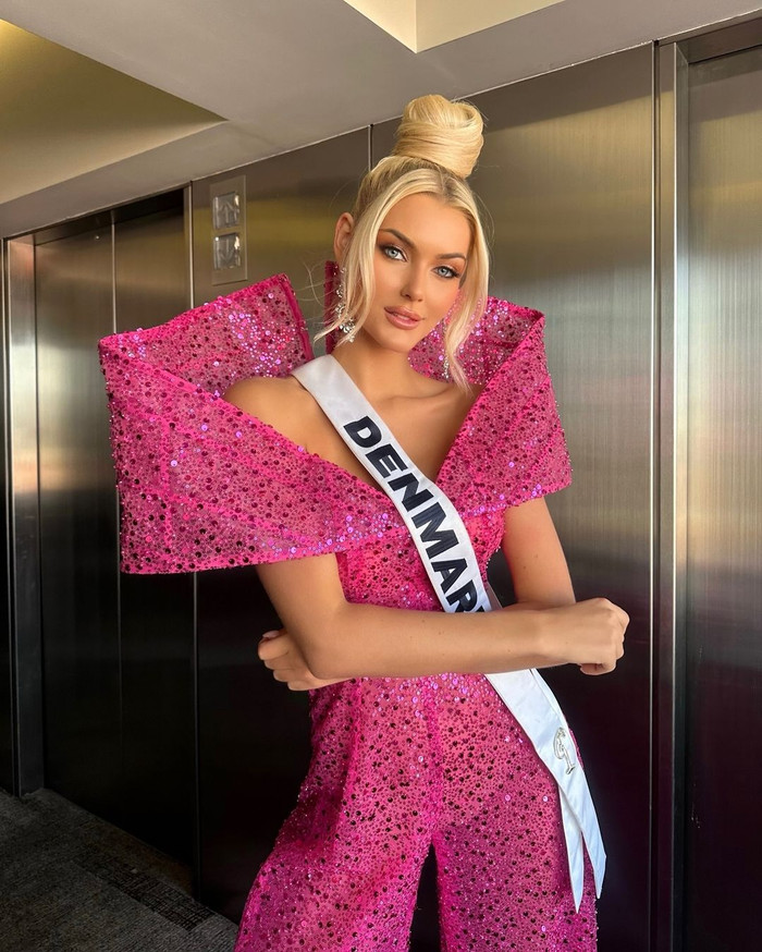 Trong một hoạt động thời điểm thi Miss Universe 2024, Victoria Kjær Theilvig gây chú ý khi diện mẫu nguyên bộ suit dài mang tồng màu hồng, đính sequins lấp lánh. Thiết kế này xẻ sâu phần ngực và ôm sát phần eo giúp người đẹp Victoria Kjær Theilvig khoe khéo vóc dáng chuẩn chỉnh. Để tăng thêm phần ấn tượng, bộ suit này thiết kế phần cầu vai phồng, mang hình dáng tựa chiếc nơ bảng lớn.