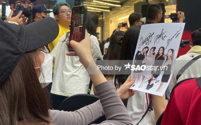 Một người hâm mộ sử dụng điện thoại để chụp lại tấm hình sở hữu đầy đủ chữ ký của bốn thành viên nhóm nhạc T-ara