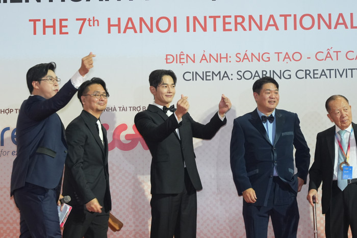 Xuất hiện tại thảm đỏ cùng với đoàn nghệ sĩ và các nhà làm phim Hàn Quốc là diễn viên On Joo-Wan (thứ 3 từ trái sang). Tài tử phim The Penthouse (Cuộc chiến thượng lưu) diện vest đen lịch lãm. Anh hào hứng giao lưu cùng khán giả hâm mộ và còn tạo dáng “bắn tim” vui vẻ.