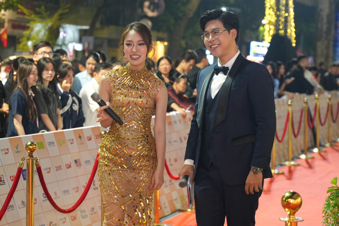 Thảm đỏ HANIFF 2024 do Khánh Vy và Vĩnh Phú chịu trách nhiệm dẫn dắt. Nữ MC diện mẫu đầm đuôi cá ôm sát người. Trên nền chất vải voan xuyên thấu, thiết kế được đính kết khéo léo bằng những hạt pha lê, hạt đá màu vàng đồng để tôn lên vòng eo của người mặc. 