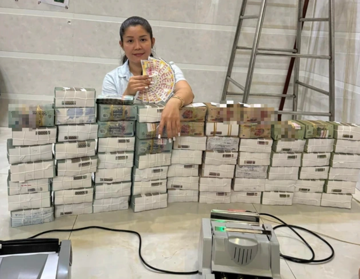 Hình ảnh người phụ nữ ngồi cạnh chồng tiền, tay cầm vé số. 