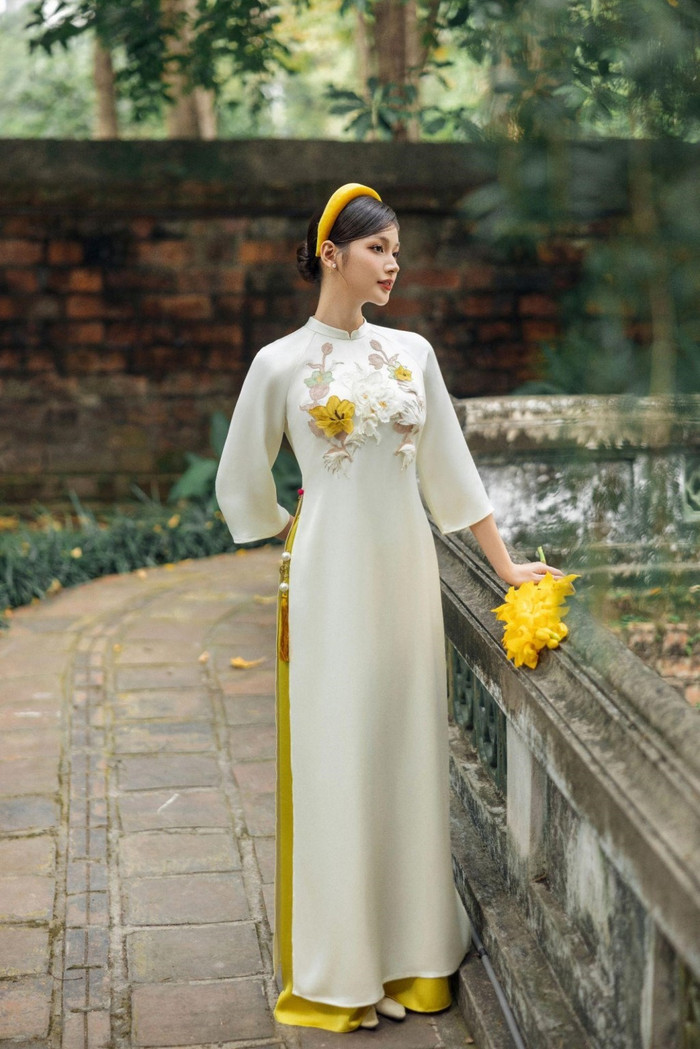 Từng chi tiết hoa đính kết trên tà áo dài không chỉ là điểm nhấn đầy nổi bật mà còn là biểu tượng của sự chăm chút và nghệ thuật thủ công tinh xảo. Mỗi bông hoa, mỗi đường kết cườm đều được thực hiện tỉ mỉ, tạo nên một tác phẩm nghệ thuật sống động trên nền vải lụa mềm mại.