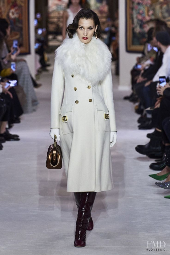 Thay vì lựa chọn những gam màu lễ hội truyền thống, Bella Hadid làm mới phong cách với chiếc áo khoác trắng dáng rộng. Cô phối áo len đỏ bó sát cùng giày cao gót quai mảnh, tạo điểm nhấn rực rỡ. Chiếc quần jeans đơn giản bên trong làm dịu đi tổng thể, mang lại vẻ ngoài hài hòa nhưng không kém phần cuốn hút. 