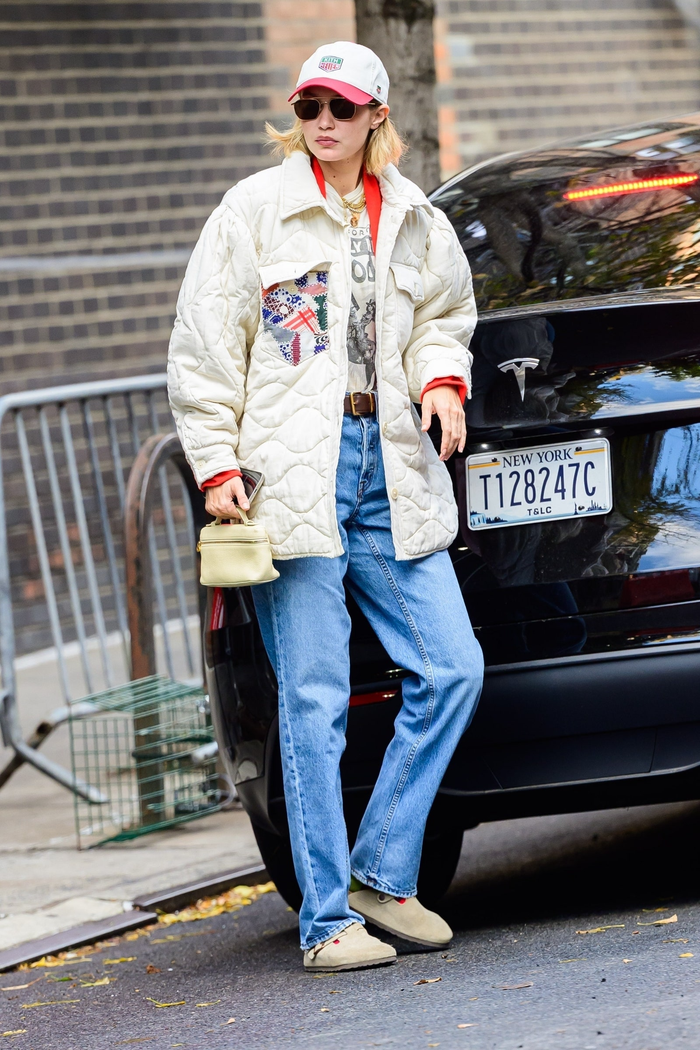 Gigi Hadid trông cực kỳ ấm áp với một chiếc áo lót chần bông màu be, phía trong có áo thun in hình kết hợp với quần jean dài cổ điển. Bên dưới, cô nàng mang thêm giày gỗ Boston bằng da lộn. 