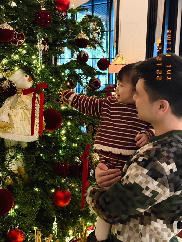 Chồng Đỗ Mỹ Linh vui vẻ bế con gái, cùng ngắm nhìn cây thông Noel. Ảnh: FBNV