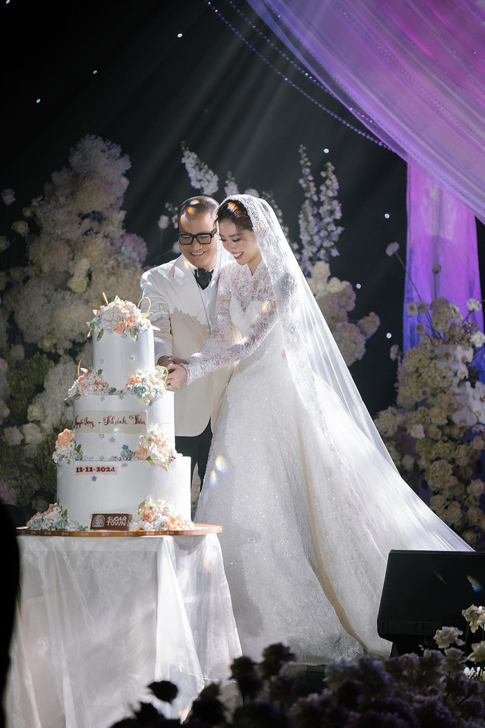 Trong phom dáng A-line cổ điển với phần cổ trụ thanh lịch được chăm chút tỉ mỉ từ từng đường kim, mũi chỉ, tôn lên vẻ đẹp thanh thoát, quý phái. Trên nền vải tulle nhẹ nhàng, chiếc váy được thêu hoạ tiết hoa ren tinh tế và điểm xuyết pha lê Swarovski lấp lánh, tựa những giọt sương ban mai đọng trên cánh hoa. Chi tiết này không chỉ tạo nên một diện mạo sang trọng mà còn gợi cảm giác thuần khiết, dịu dàng đầy cuốn hút. Để hoàn thiện diện mạo cho cô dâu, Lê Thanh Hòa kết hợp cùng chiếc veil đặc biệt, được điểm xuyết bởi những bông hoa cánh bướm đính kết thủ công.