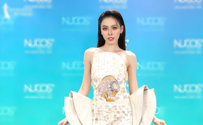 Á hậu Ngọc Hằng nổi bật với phong cách thời trang hiện đại và sáng tạo. Bộ trang phục lấp lánh ánh ngọc trai được thiết kế tinh xảo với các mảng vuông đan xen. Điểm nhấn chính là phần eo được cắt hở táo bạo, trang trí bằng họa tiết thêu tay tinh tế. Hai bên tay váy cách điệu với những đường gấp lớn mang lại vẻ quyền lực và cuốn hút. Sự tự tin và thần thái mạnh mẽ của Ngọc Hằng đã biến bộ trang phục trở thành tâm điểm chú ý.