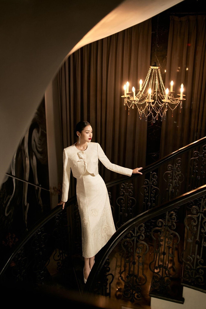 Thiết kế thạch lịch với gam màu trắng ngà, đầm kết hợp thành công giữa ba yếu tố cốt lõi: cổ tròn, tay vòm, dáng đuôi cá để tôn lên vẻ đẹp của người mặc, tạo ra sự ấn tượng, đem đến một vẻ đẹp quyến rũ và tự tin.