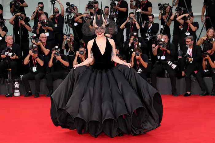 Mọi ánh mắt đều đổ dồn khi Lady Gaga bước lên thảm đỏ tại Liên hoan phim Venice để quảng bá cho bộ phim Joker: Folie à Deux. Cô diện một thiết kế couture đặt riêng từ Dior. Chiếc váy này hoàn toàn khác biệt so với phong cách tối giản thường thấy của Dior, với phần cổ xẻ sâu táo bạo và chân váy phồng tựa như một tác phẩm nghệ thuật origami. Bộ vòng cổ kim cương dạng quai từ Tiffany & Co và chiếc mũ đội đầu ren đen đầy ma mị, mang phong cách Nosferatu, được thiết kế bởi Philip Treacy. 