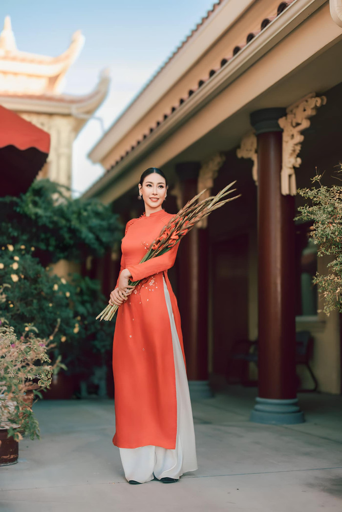 Xuất hiện trong ống kính, nàng hậu khoe sắc với tà áo nhuộm gam đỏ cam, thêu hoa lá phối cùng họa tiết vô cùng nổi bật. Cô còn sắm thêm bó hoa huệ đỏ giúp tô điểm cho toàn cảnh.