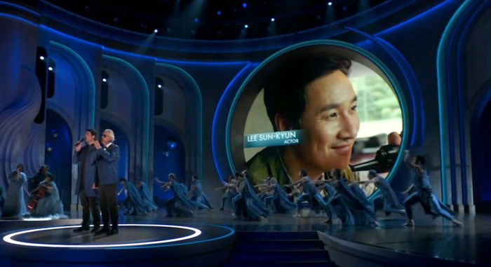 Trong khi các nghệ sĩ biểu diễn nhạc phẩm, trên màn hình là chân dung các nhà sản xuất, đạo diễn, diễn viên và người làm trong nền công nghiệp Hollywood qua đời năm ngoái, trong đó có tài tử Hàn Lee Sun Kyun.