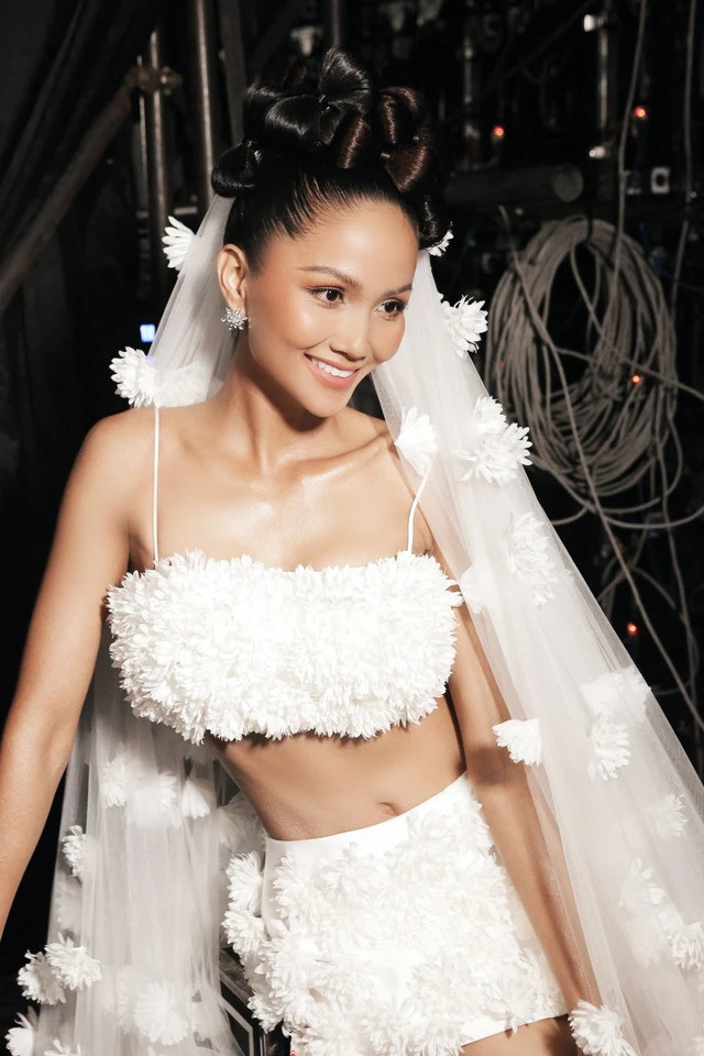 H'Hen Niê trông cực kỳ quyến rũ với chiếc váy cưới được kết hợp từ áo croptop 2 dây và váy ngắn. Phần vải voan trùm đầu được đính thêm những bông hoa trắng khiến tổng thể thiết kế trông cực kỳ thu hút. Ngoài ra, hình thể chuẩn không cần chỉnh của H'Hen Niê cũng giúp cho thiết kế trở nên nổi bật hơn.