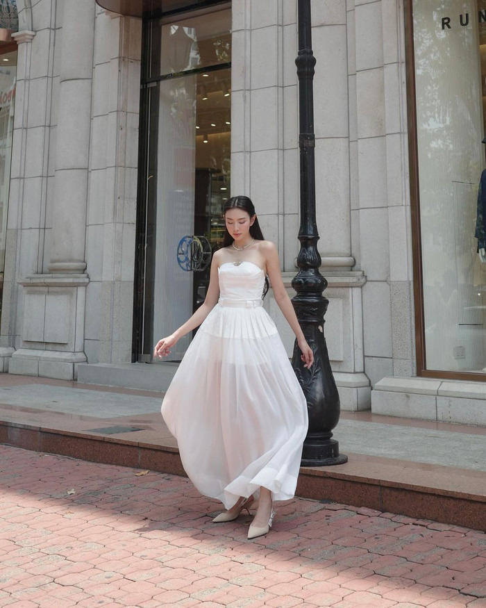 Hình ảnh quý cô thanh lịch được Thùy Tiên thể hiện qua midi dress mang hơi hướm business core nhuộm tông trắng. Đường kéo khéo léo kết hợp kỹ thuật chiết eo tạo nên sihouette cho tổng thể. Phần corset ôm theo đường vòng cung được cắt may trên nền vải kaki dày dặn. Được biết, mẫu váy mang tên Pandora, nằm trong BST xuân hè 2024 của nhà mốt Dear José. Hiện tại, thiết kế được bán ra với giá gần 2,5 triệu. Có thể thấy, cô tiếp tục trưng dụng mẫu giày J’ Aior Slingback Pump (hơn 25 triệu) cho buổi chụp ảnh phố phường.