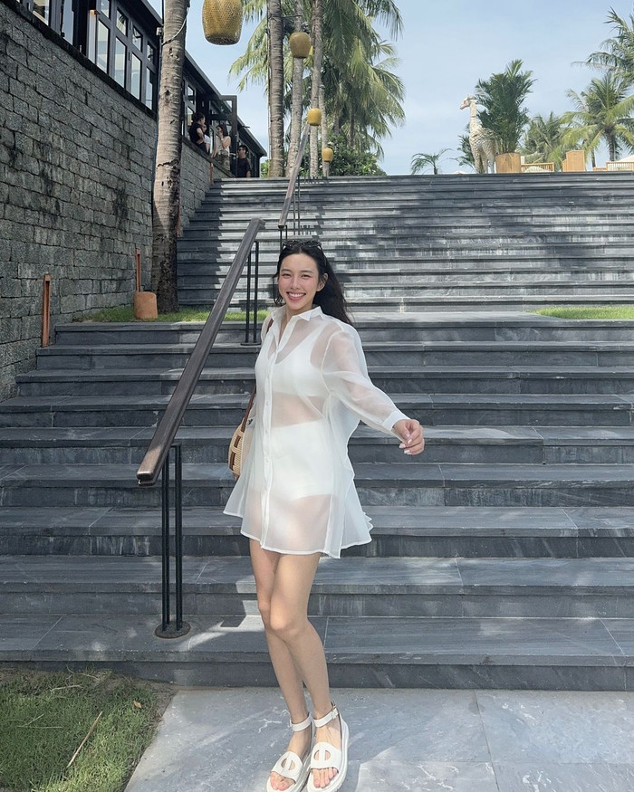 Người đẹp sinh năm 1998 khoe trọn hình thể săn chắc trong bản phối xuyên thấu nhuộm tông trắng đến từ nhà mốt Dala Studios. Chất liệu thun co giãn thoáng khí ở mẫu croptop và quần giúp ôm trọn và tôn lên số đo ba vòng của cô. Sẽ thật thiếu xót nếu đôi giày da bò D-Club Sandal không được nàng hậu thêm vào danh sách items cho tạo hình lần này. Được biết, mẫu thiết kế được nhãn hàng trình làng giới mộ điệu với giá hơn 40 triệu đồng. Phù hợp với không khí mùa hè, người đẹp diện chiếc túi đan Loewe beehive anagram raffia basket shoulder bag có giá khoảng 31 triệu đồng.