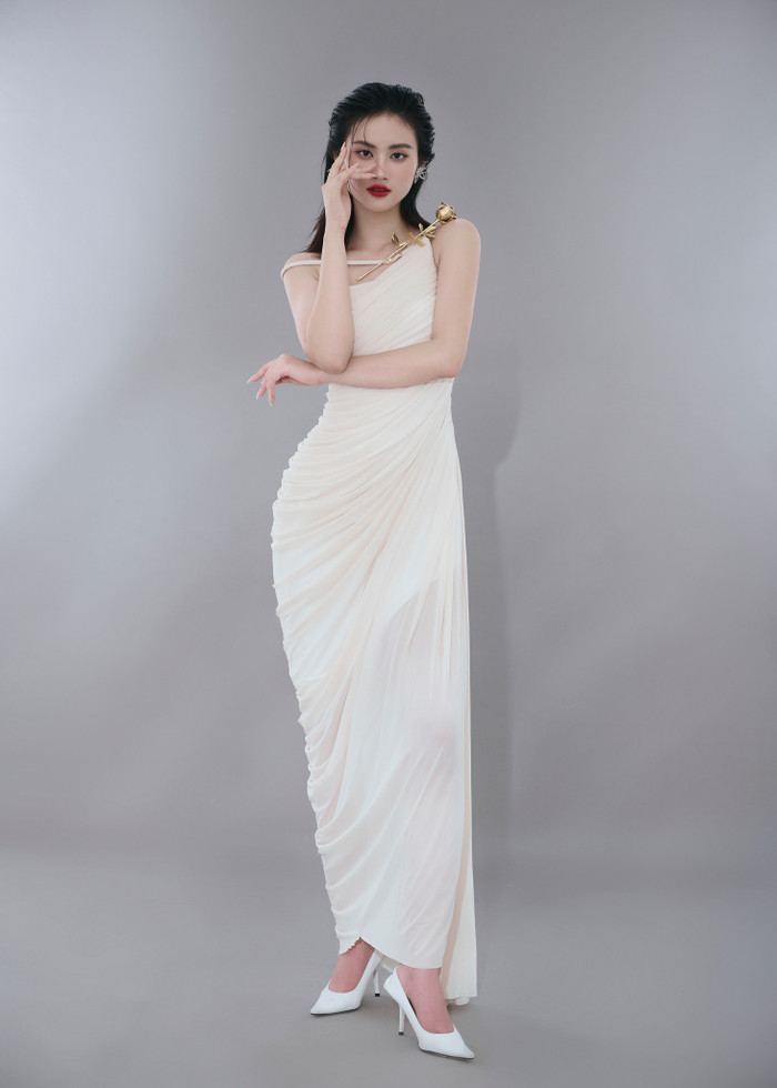 Một lần khác, Hoa hậu Ý Nhi diện mẫu váy trắng dài, chất liệu mềm mại. Thiết kế này còn được tạo đính cành hoa hồng mạ vàng trên phần vai. Hoa hậu Ý Nhi khéo léo tạo kiểu tóc ướt át, tém gọn ra phía sau kết hợp cùng phong cách trang điểm đậm, kết hợp với đôi môi đỏ căng mọng tăng thêm phần quyền lực, quyến rũ.