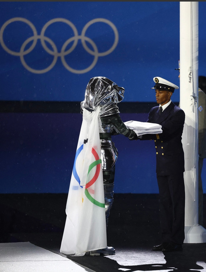 Cờ Olympic được người giấu mặt trao cho đội nghi thức trước lễ thượng cờ - Ảnh: REUTERS.