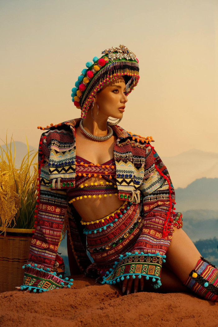 Về chất liệu, bộ trang phục này làm hoàn toàn bằng thổ cẩm được dệt từ những đôi bàn tay khéo léo của người dân đồng bào Tây Bắc, có màu sắc sặc sỡ và hoạ tiết đặc trưng. Thiết kế có phần nón được đính kết các chi tiết tua rua bắt mắt, phần tà được làm dài sang hai bên tạo cảm giác cân đối cho người mặc. 