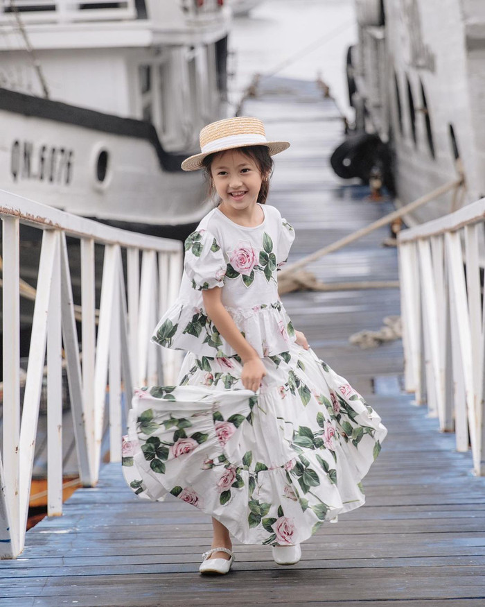 Trong một lần khác, con gái Hoa hậu Hà Kiều Anh diện chiếc váy xếp ly trắng bồng bềnh, ngọt ngào tựa công chúa. Thiết kế này còn được tạo điểm nhấn bằng loạt hoạ tiết hoa hồng tôn lên sự đáng yêu của nàng ái nữ. Mẫu váy này được bán với mức giá khoảng 15 triệu đồng. Huỳnh Viann còn phối cùng giày bệt trắng và nón cói rộng vành.
