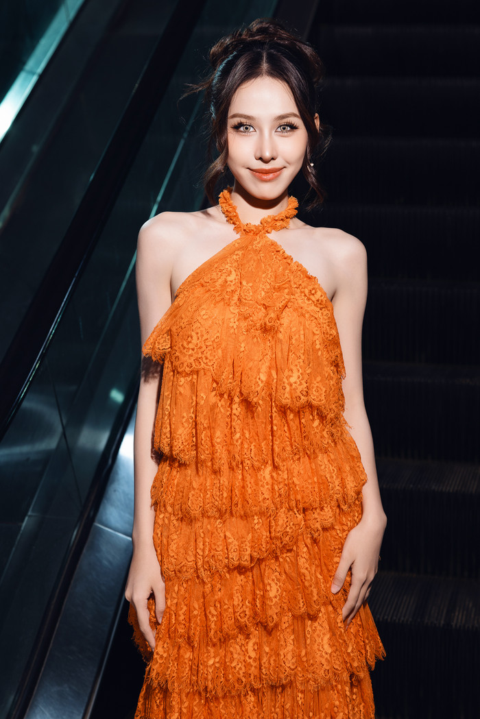 Á hậu Ngọc Hằng gây ấn tượng với màu mắt nâu olive với mái tóc búi gọn. Cô diện đầm cổ yếm chất ren, may dáng rũ layer. 