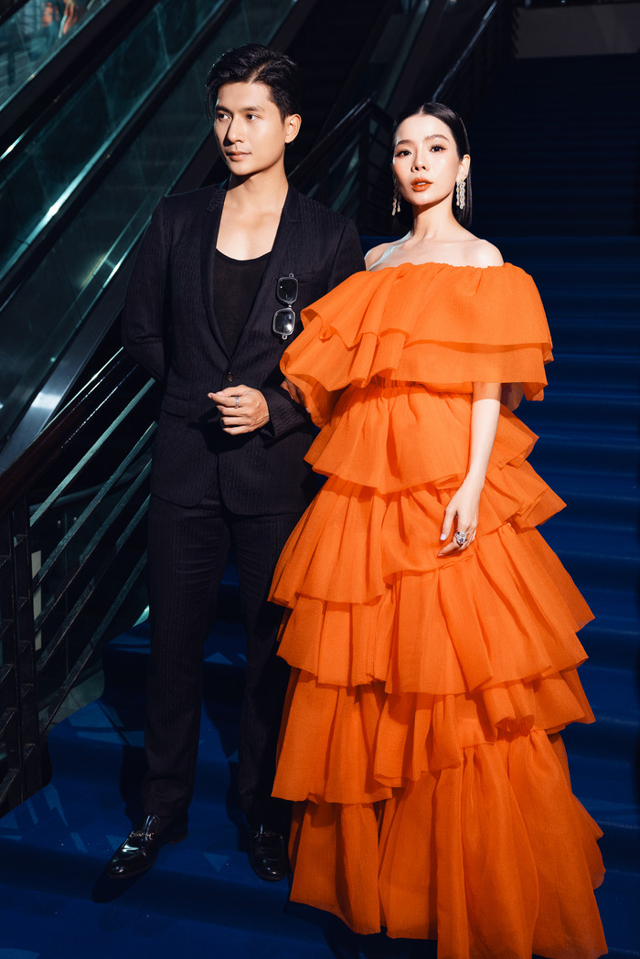 Lệ Quyên và bạn trai Lâm Bảo Châu diện hai màu đen và cam đúng tinh thần dresscode của show diễn. Chiều cao của nữ ca sĩ trở nên nổi bật với chiếc váy trễ vai may dạng layer, giọng ca sinh năm 1982 không phối thêm phụ kiện để tổng thể sang trọng, đơn giản hơn.