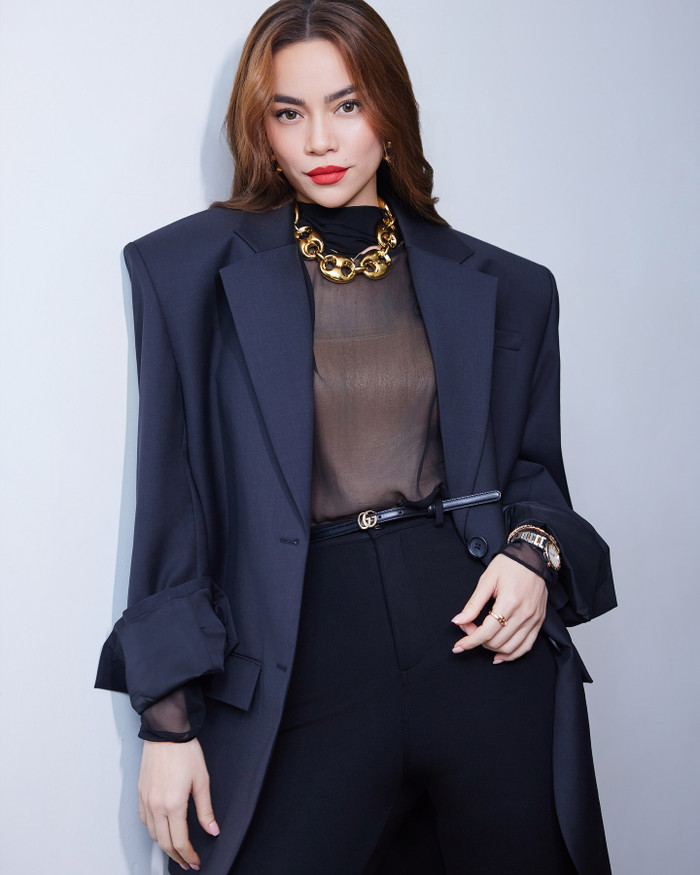 Hồ Ngọc Hà hoá thân thành quý cô quyền lực trong bộ vest đen, đứng form. Tuy nhiên, nữ ca sĩ vẫn giữ vững phong thái quyến rũ, mặn mà khi kết hợp cùng chiếc áo thun xuyên thấu. Để thêm phần thu hút, Hồ Ngọc Hà khéo léo chọn lựa phong cách trang điểm đậm, nhấn nhá bằng đôi môi đỏ tươi ấn tượng và mái tóc uốn bồng bềnh, gợn sóng.