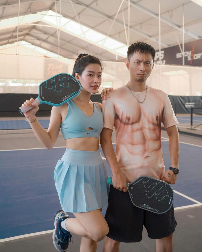 Vợ chồng hot girl Hạt Mít và rapper Rhymastic khiến người hâm mộ phì cười với hình ảnh tình tứ trên sân pickleball. Trong khi vợ diện set đồ mát mẻ kết hợp giữa bra-top với váy màu xanh da trời, anh chàng rapper lại diện áo thun có hình cơ bắp cực hài hước. 