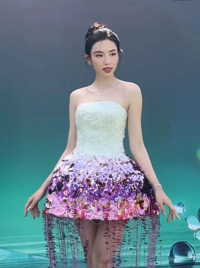 Hoa hậu Thùy Tiên khoác lên người mẫu váy ngắn cúp ngực, hiệu ứng tua rua. Thiết kế này giúp cựu Miss Grand International khoe trọn đôi chân dài nuột nà, không chút khuyết điểm cùng phần xương quai xanh góc cạnh, quyến rũ. Không những vậy, cô còn kết hợp với layout trang điểm nhẹ nhàng, theo tông màu hồng chủ đạo. Tổng thể tạo hình của Hoa hậu Thùy Tiên được ví von như nàng công chúa bước ra từ truyện cổ tích.