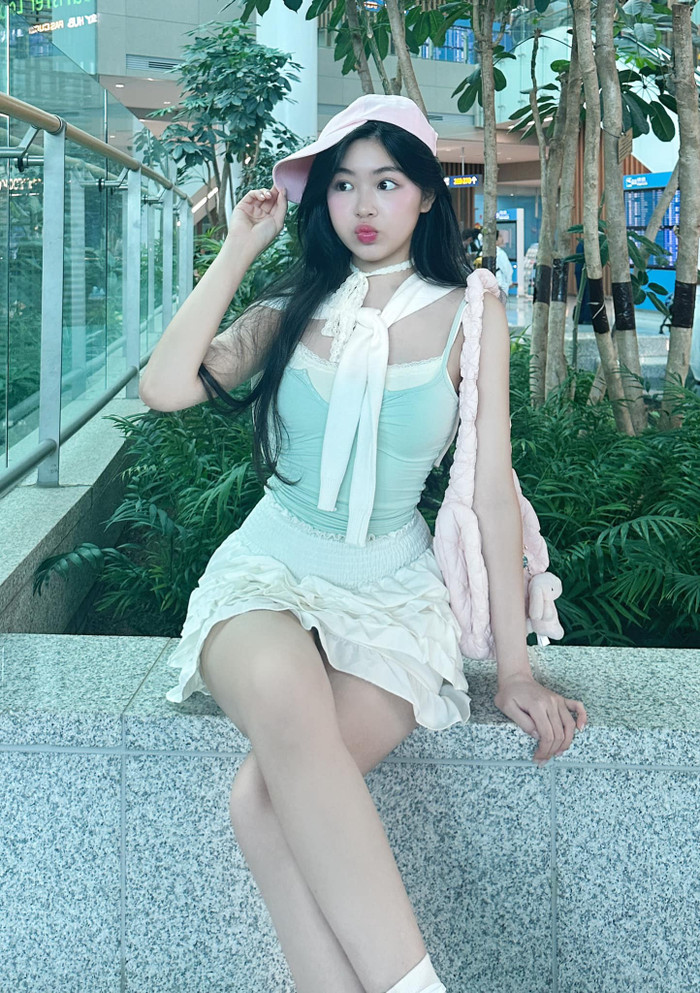 Con gái Quyền Linh diện mẫu váy ngắn cũn, chi tiết bèo nhún cùng chiếc áo hai dây chất liệu mềm mại, ôm sát. Về phụ kiện, Lọ Lem phối cùng nơ đeo cổ, nón lưỡi trai và giỏ xách đồng màu hồng pastel ngọt ngào. Cô nàng còn hoà nhập xu hướng thời trang đang thịnh hành thông qua việc đính móc khoá thú cưng như một món charm túi xách. Bản phối gồm hai màu sắc xanh lá pastel và hồng pastel của Lọ Lem được đánh giá 'cao tay', đem lại sự dễ chịu, mát mắt.