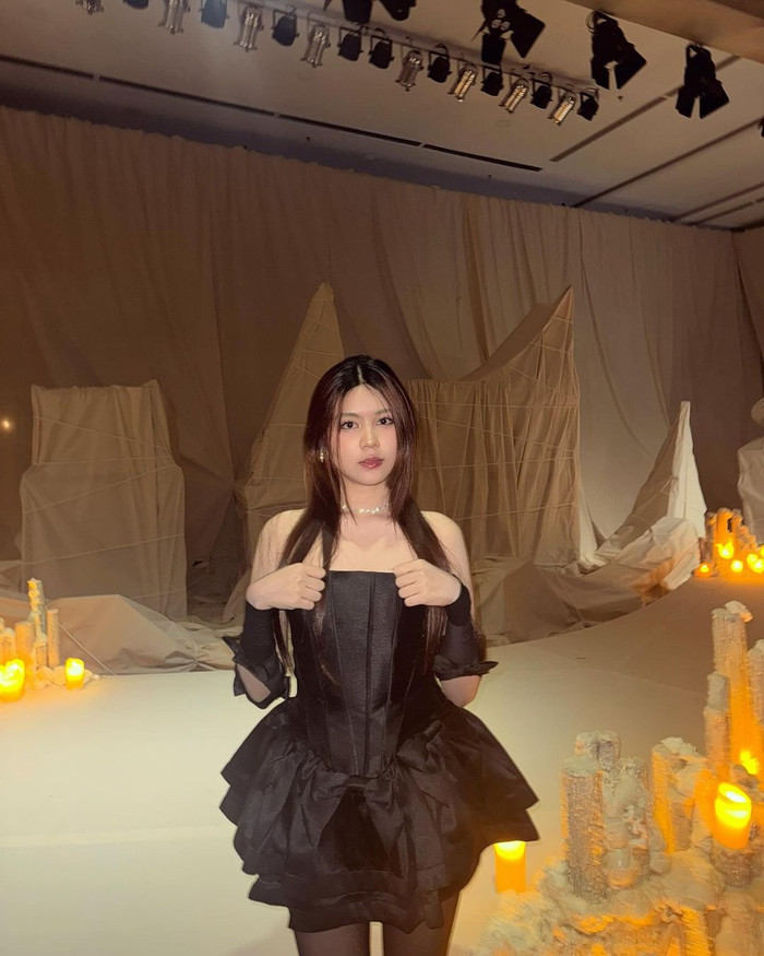 Hạt Dẻ thu hút ánh nhìn với bản phối corset và tùng váy xòe phân tầng độc đáo. Không chỉ giúp tôn lên tỉ lệ hình thể, phần ống áo còn giúp người mặc khoe khéo khung xương quai xanh thanh mảnh.  Sắc đen tô điểm không khiến cho vẻ ngoài cô trở nên “đứng tuổi”, trái lại hình ảnh còn thêm phần ấn tượng. Đi kèm thiết kế, quý nữ nhà Quyền Linh phối  phụ kiện đeo tay thắt nơ xinh xắn.  